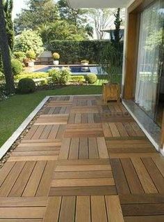 a wooden deck in front of a house with grass and trees on the other side