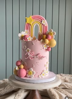 a pink birthday cake decorated with balloons and a rainbow