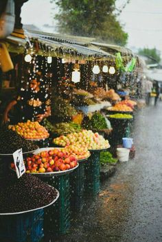 an open air market with fruits and vegetables on the tables under umbrellas in the rain