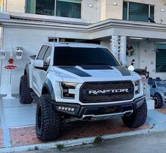 a white and black truck parked in front of a building with large tires on it