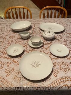 a table topped with lots of white plates and bowls on top of a lace covered table cloth