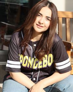 a young woman sitting on top of a wooden bench wearing a baseball uniform and smiling at the camera