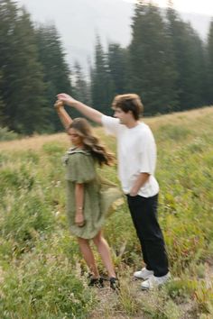 a man and woman standing in a field with trees in the background