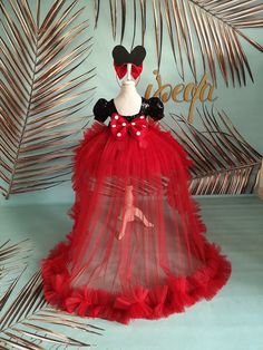 a red tulle skirt with minnie mouse ears and black bows on the top, sitting in front of a palm tree