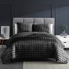 a bed with black comforter and pillows on top of it in a gray room