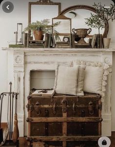 an old trunk sitting in front of a fireplace with pillows and other items on top