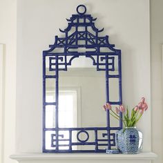 a blue and white mirror sitting on top of a shelf next to a vase with flowers