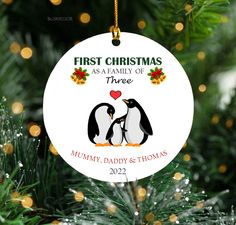 a christmas ornament with two penguins kissing on it's face and the words, first christmas as a family of three