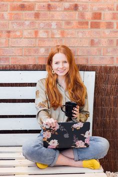 a woman sitting on a bench holding a laptop computer and smiling at the camera with her legs crossed