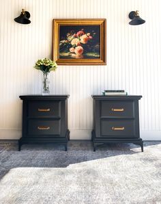 two black nightstands in front of a wall with flowers on it and a painting above them