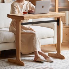 a woman sitting at a table with a laptop computer on her lap and holding a drink