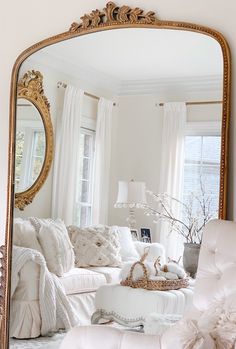 a living room filled with furniture and a large gold framed mirror over the couches