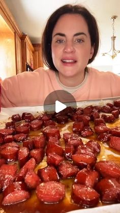 a woman is looking at the camera while she holds up a baking pan full of food