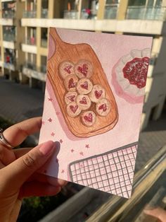 a hand holding up a card with some food on it and buildings in the background