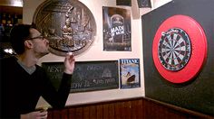 a man drinking from a glass in front of darts and darts on the wall