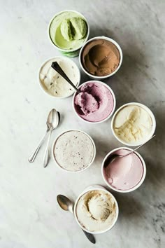 five bowls of ice cream with spoons on a marble surface, all in different colors