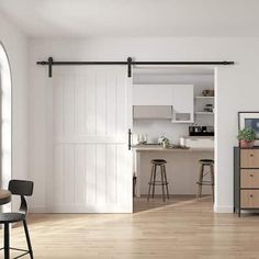 an open kitchen and living room with white walls, wood floors and sliding barn doors