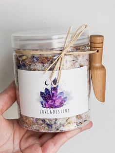 a hand holding a jar of lavender and basil bath salts in front of a white wall