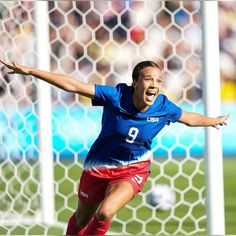 a female soccer player in action on the field with her arms out and mouth wide open