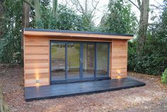 a small wooden building in the middle of a forest with doors open and lights on