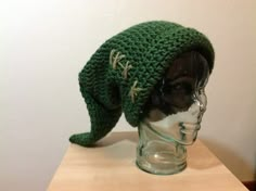 a green knitted hat sitting on top of a glass head mannequin's head