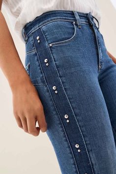 a woman is wearing jeans with buttons on the side and her hands in her pockets