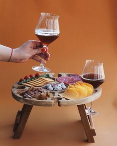 a person holding a wine glass over a tray with cheeses and crackers