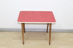 a small red table sitting on top of a hard wood floor next to a white wall