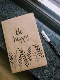 a notebook with the words be happy written on it next to a pen and window sill