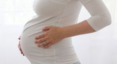 a pregnant woman in white shirt holding her stomach