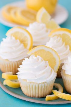 lemon cupcakes with white frosting and sliced lemons on the side, sitting on a plate