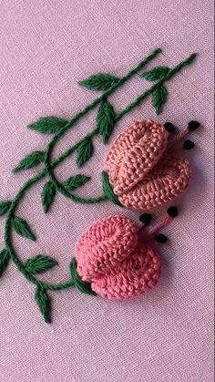 two crocheted flowers on a pink surface with green leaves and buds, one is in the shape of an ornament