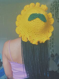 a woman with long black hair wearing a yellow crochet sunflower hat on her head