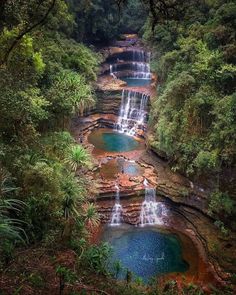 several waterfalls in the middle of a forest with blue pools surrounded by trees and greenery