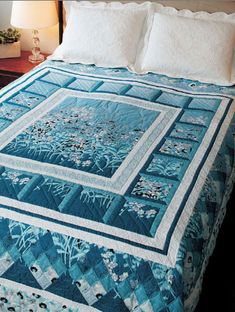 a bed with blue and white quilted bedspread on top of it next to a night stand