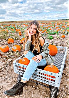 a woman sitting on a crate in a pumpkin field