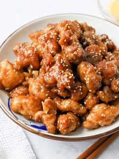 a white plate topped with chicken covered in sesame seeds next to chopsticks and sauce