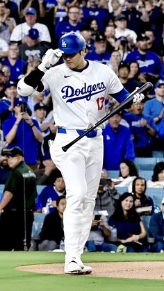 a dodgers baseball player walking off the field with his bat in hand and fans behind him