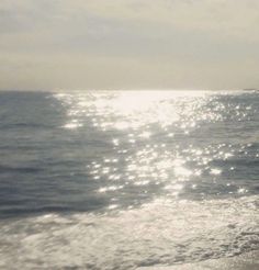 a person walking on the beach with a surfboard in their hand and sunlight reflecting off the water