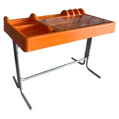 an orange table with a glass top and metal legs on one side, in the shape of a dog's paw