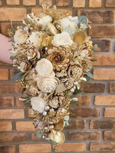 a bridal bouquet made up of gold and white flowers on a brick wall in front of a woman's hand