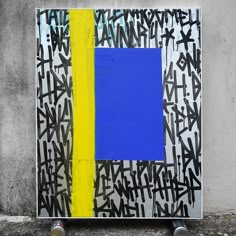 a person standing in front of a painting on the side of a building with blue, yellow and black paint