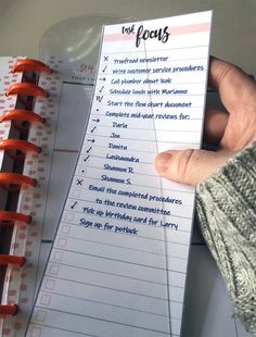 a hand holding a notepad with writing on it next to a spiral binder