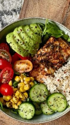 a bowl filled with rice, vegetables and meat on top of a wooden table next to a fork