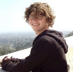 a young man sitting on top of a cement wall next to a lush green hillside