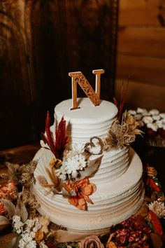 a white wedding cake with the letter n on top is surrounded by flowers and feathers