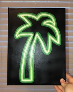 a hand holding up a black and green sign with palm trees on it's side