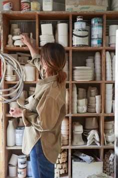 a woman standing in front of a shelf filled with white dishes