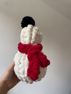 a hand holding a crocheted snowman ornament in red and white