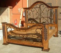 a wooden bed frame with iron work on the headboard and foot board, in front of a building